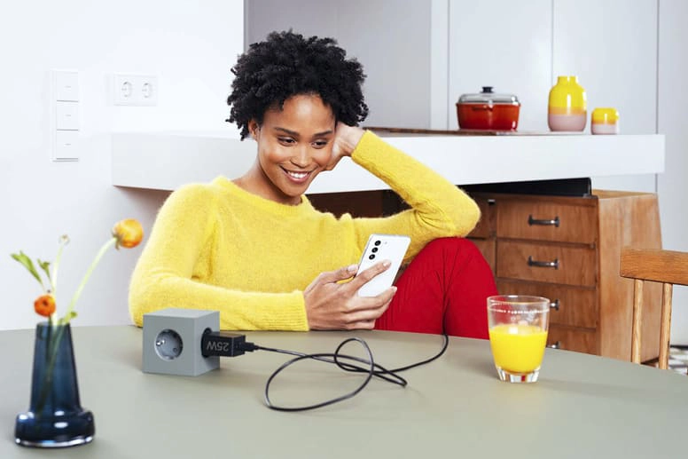 Young woman sits with a Samsung fast charger on the table and smiles towards her smartphone.