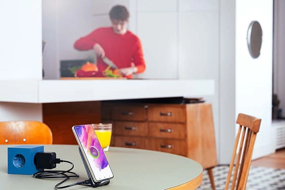 A teenager cooks in the background, while a Samsung smartphone charges in the inductive charging station on the table.