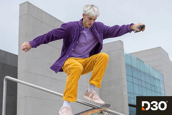 Skater jumps over a railing outdoors and holds his smartphone.