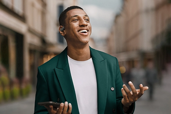 Man standing in the city with open arms, talking on his smartphone with Hama Bluetooth headphones ‘Spirit Open’.