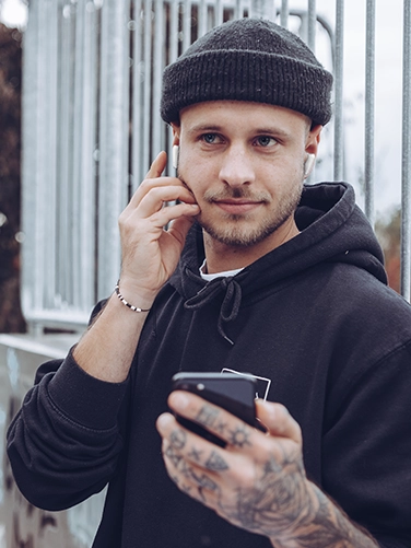 Young man wearing the Hama "Spirit Pocket" Bluetooth headphones and operating his cell phone