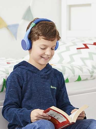A boy sits in his room and reads a book while wearing the Hama Bluetooth® headphones "Teens Guard"
