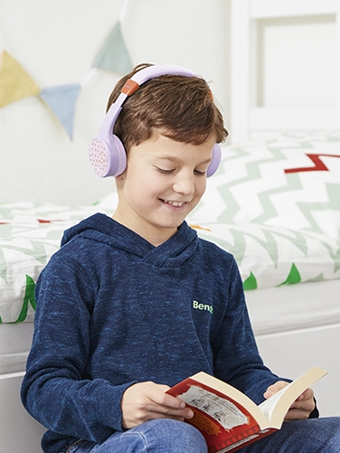 A boy sits in his room and reads a book while wearing the Hama Bluetooth® headphones "Teens Guard II"