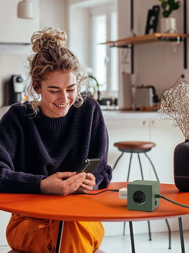 Young woman sitting at a dining table and operating her smartphone while it is being charged with the Hama fast charger, 20W