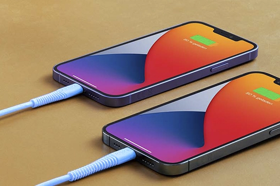 Two iPhones lie on a table and are charged with the "Flexible" charging cable.