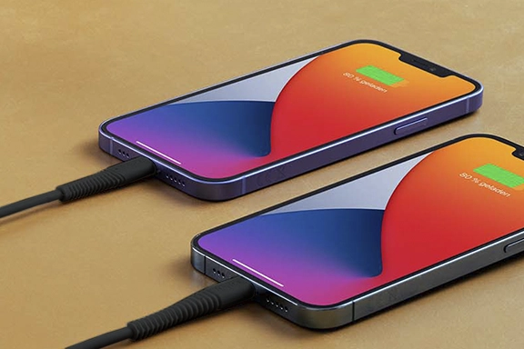 Two iPhones lie on a table and are charged with the "Flexible" charging cable.