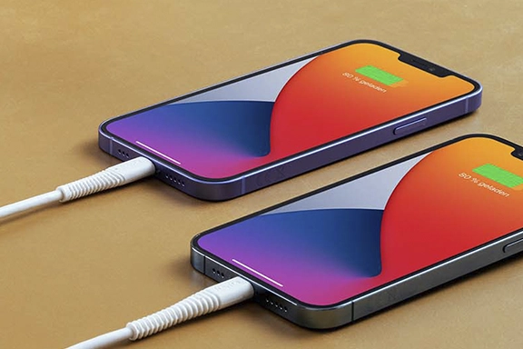 Two iPhones lie on a table and are charged with the "Flexible" charging cable.