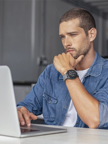 A man works on his laptop in the office with his smartwatch on his arm