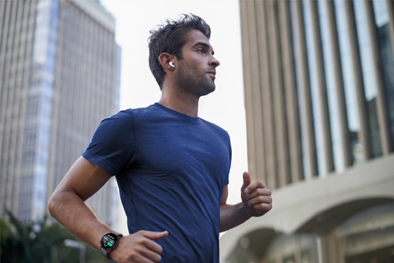 Man jogs through the city with headphones in his ear and smartwatch in his hand