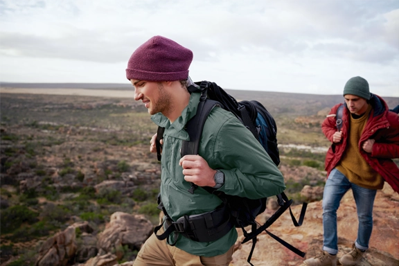 2 men hike through the mountains with a fitness watch on their hands, which supports GPS.