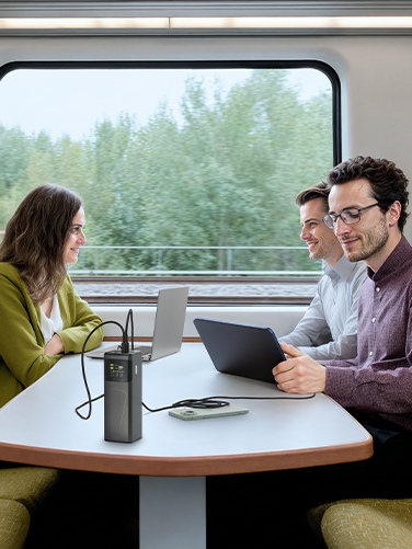 Three adults are sitting on a train. A man is charging his tablet with a power pack. 