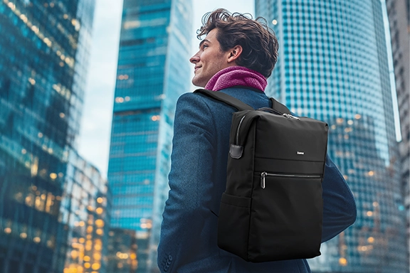 A young man stands in a big city with modern tower blocks. He is carrying the ‘Ultimate’ laptop rucksack on his back