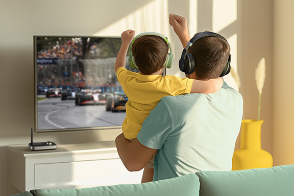 Father and son are sitting on the sofa and cheering on a Formula 1 race - but very quietly, because they are listening to the sound through headphones connected via the Hama Bluetooth® adapter "Link.it duo"